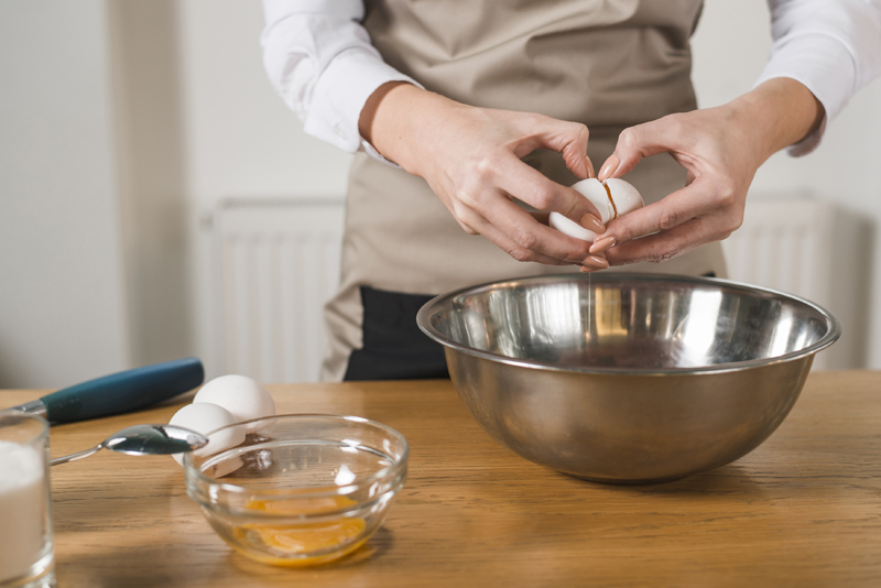gros-plan-femme-main-casser-oeuf-bol-melangeur-table-bois